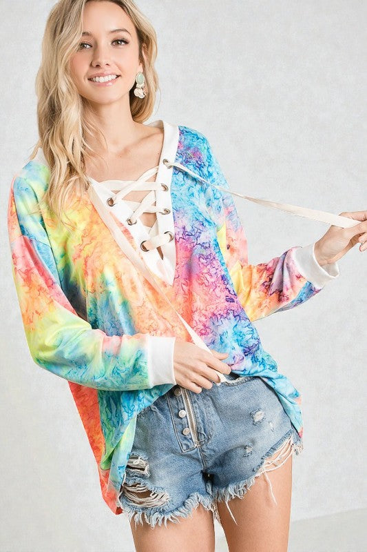 Woman wearing a colorful tie-dye cardigan over a white lace top with denim shorts on a plain background