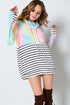 Woman wearing a colorful tie-dye hoodie over a striped dress with brown boots on a white background
