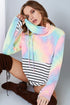 Woman wearing a colorful tie-dye hoodie with a striped shirt underneath, sitting on the floor.