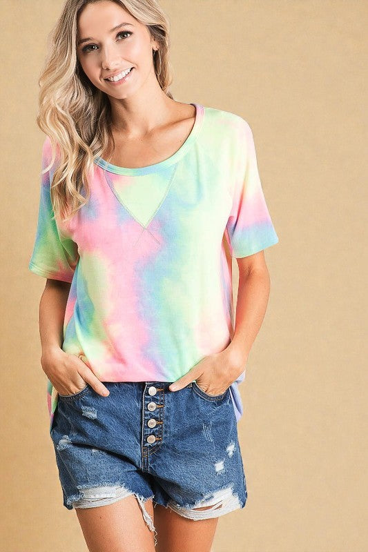 Woman wearing a tie-dye shirt and denim shorts on a beige background