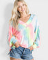 Woman wearing a colorful tie-dye shirt and denim shorts on a plain background