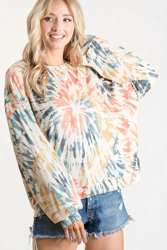 Woman wearing a tie-dye long-sleeve shirt and denim shorts on a white background