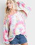 Woman wearing a colorful tie-dye long-sleeve top and denim shorts on a plain background