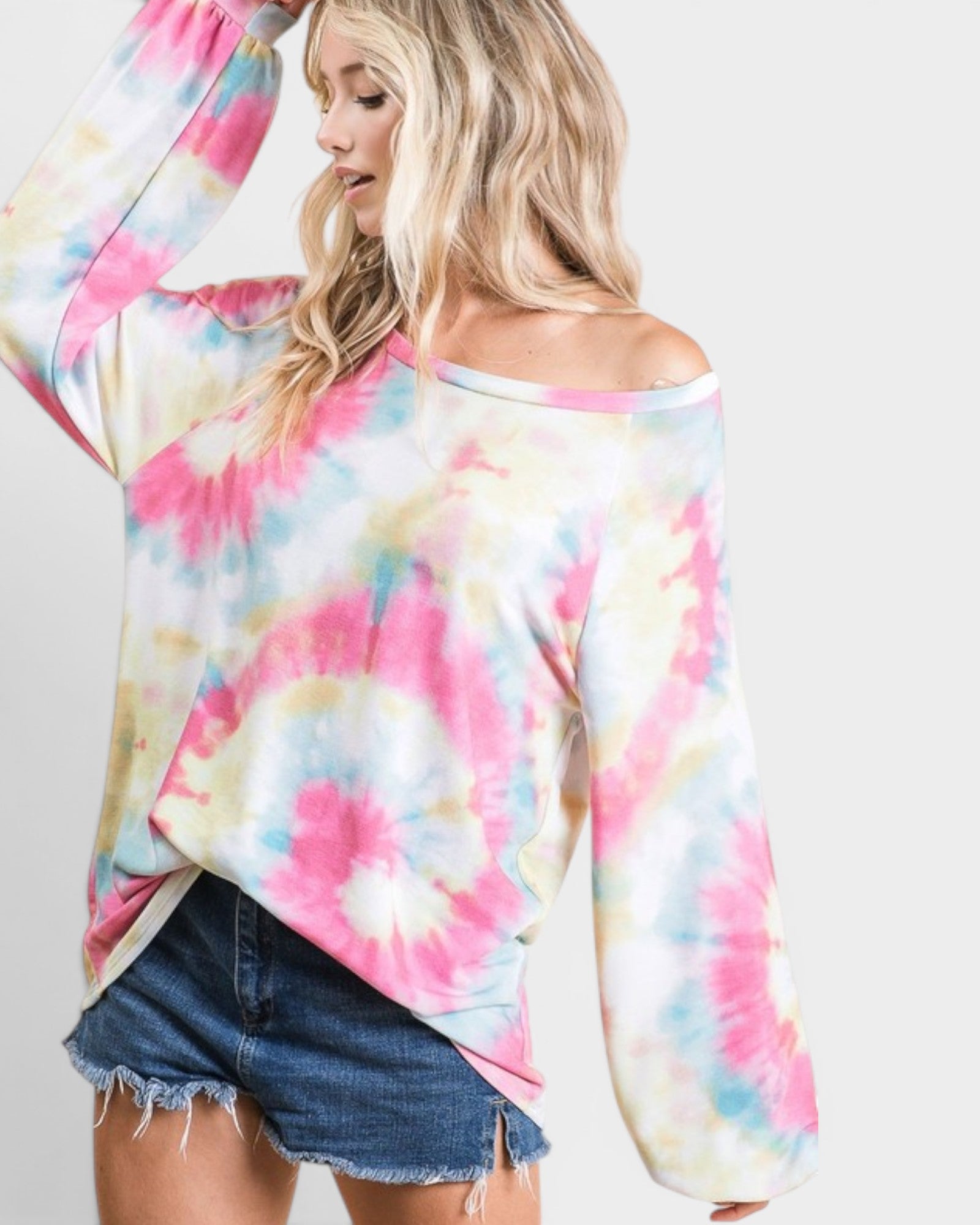 Woman wearing a colorful tie-dye long-sleeve top and denim shorts on a plain background