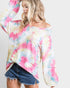Woman wearing a colorful tie-dye long-sleeve top and denim shorts on a plain background