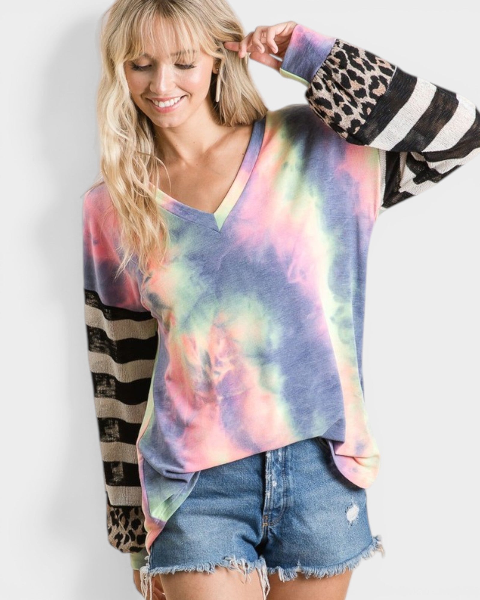 Woman wearing a tie-dye long-sleeve top with a colorful pattern, denim shorts, and a striped jacket.