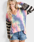 Woman wearing a tie-dye long-sleeve top with a colorful pattern, denim shorts, and a striped jacket.