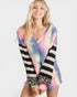 Woman wearing a colorful striped and tie-dye top with leopard print accents on a white background