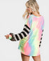 Woman wearing a colorful tie-dye dress with black and white striped sleeves on a plain background