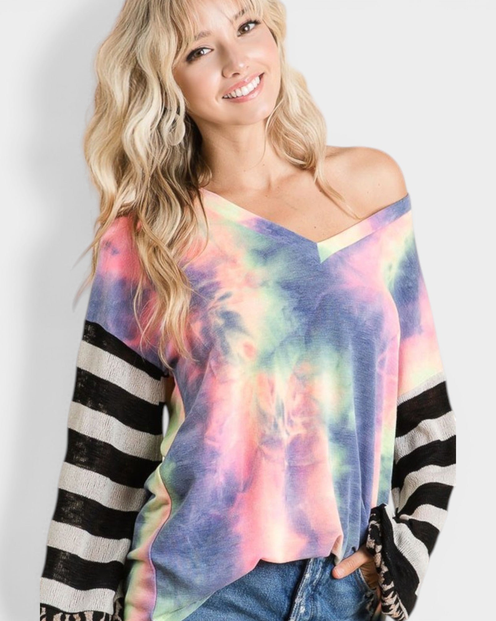 Woman wearing a colorful tie-dye sweater with black and white striped sleeves on a plain background