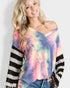 Woman wearing a colorful tie-dye sweater with black and white striped sleeves on a plain background