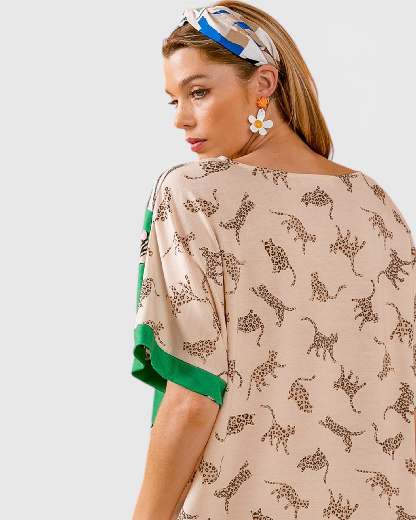 Woman wearing a beige patterned top with green sleeves on a plain background