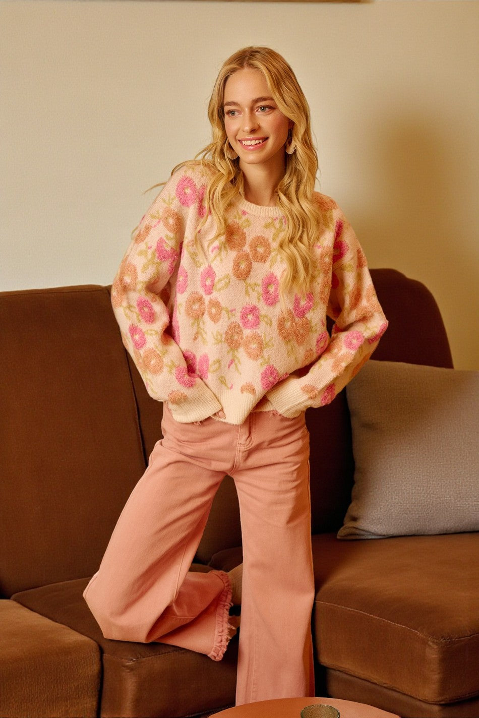 Woman wearing a floral sweater and pink pants sitting on a brown couch.