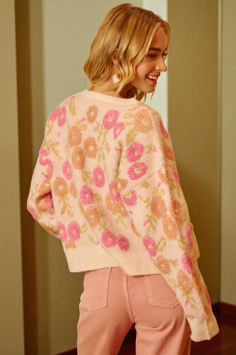 Woman wearing a floral patterned sweater and pink pants indoors.