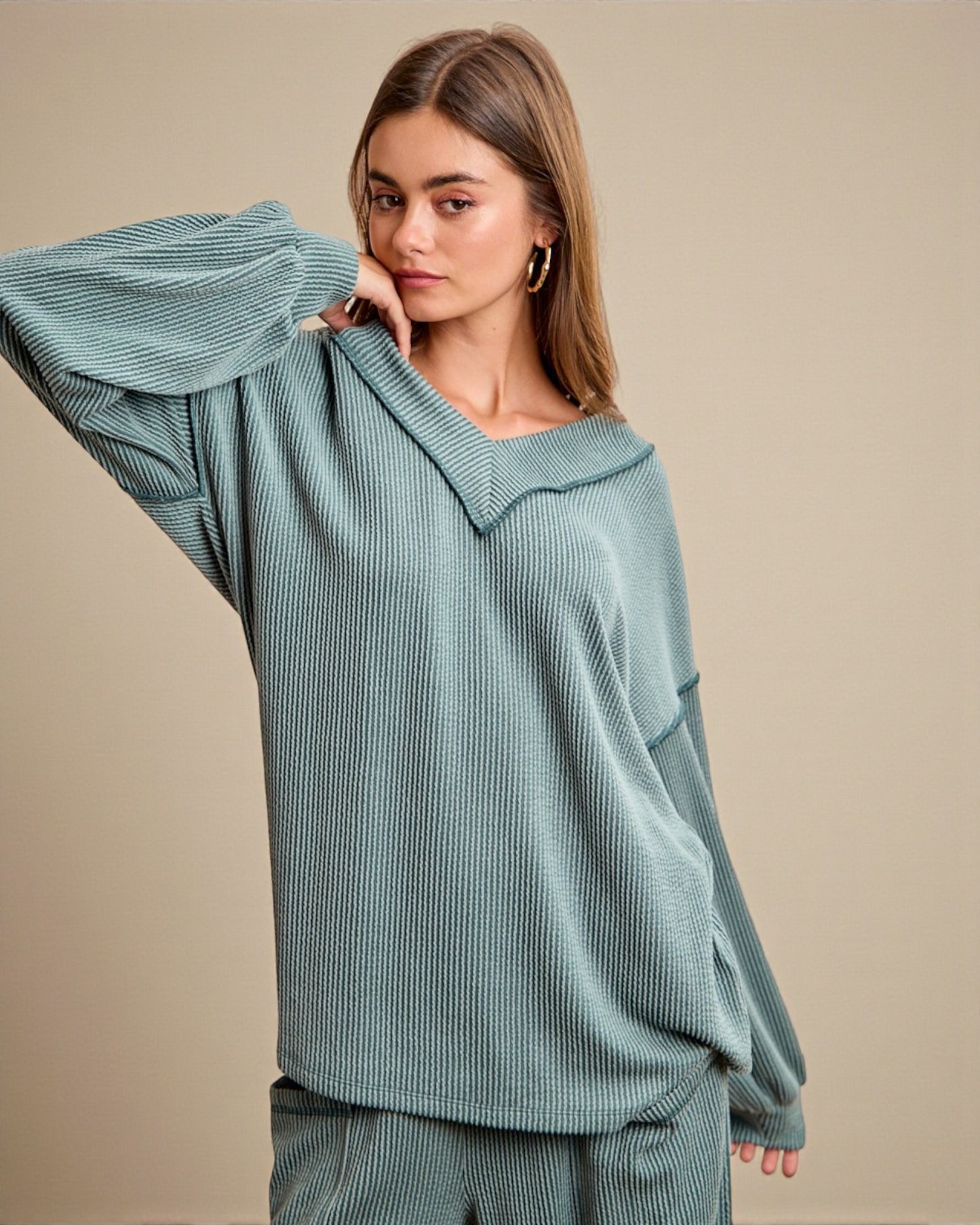 Woman wearing a teal ribbed sweater against a beige background