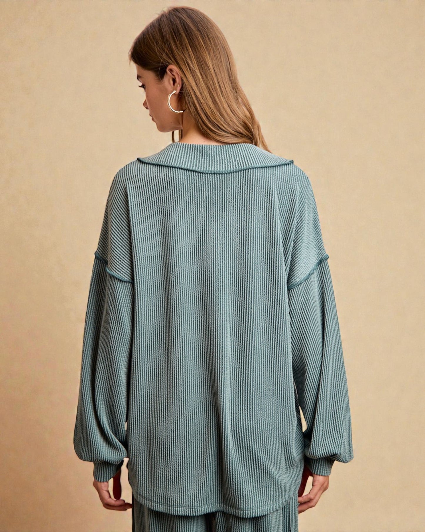 Woman wearing a teal ribbed sweater and pants on a beige background