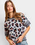 A woman wearing a short-sleeve knit sweater with a leopard print pattern in black, brown, and beige, featuring striped ribbed cuffs and hem, paired with blue jeans against a light gray background.