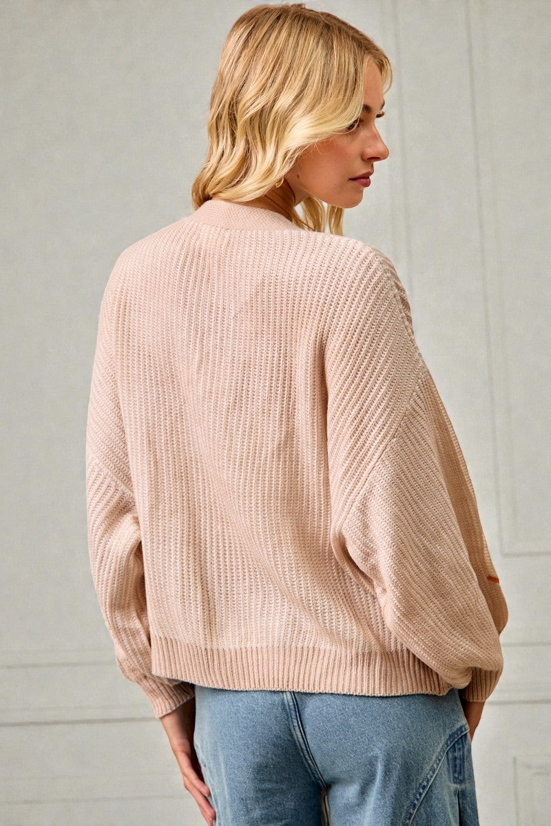 Woman wearing a beige sweater and blue jeans against a light background