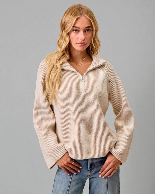 Woman wearing a beige ribbed sweater with a zipper on a gray background