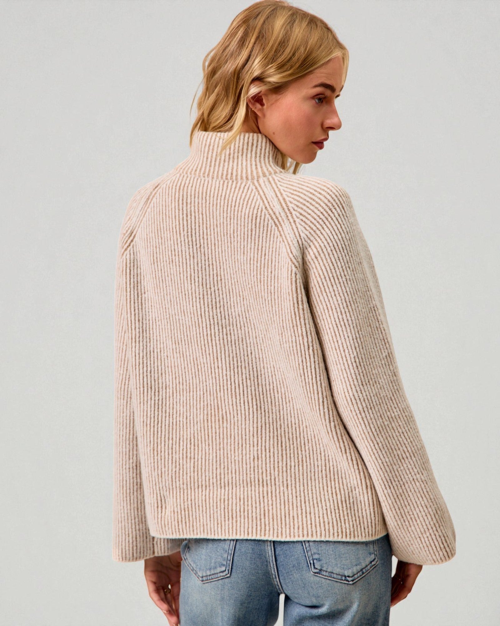 Woman wearing a beige ribbed sweater against a plain background