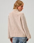 Woman wearing a beige ribbed sweater against a plain background