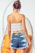 Woman wearing a white strapless top and denim shorts sitting on a white chair with an orange cushion.