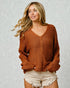 Woman wearing a brown sweater and white shorts against a textured light gray background