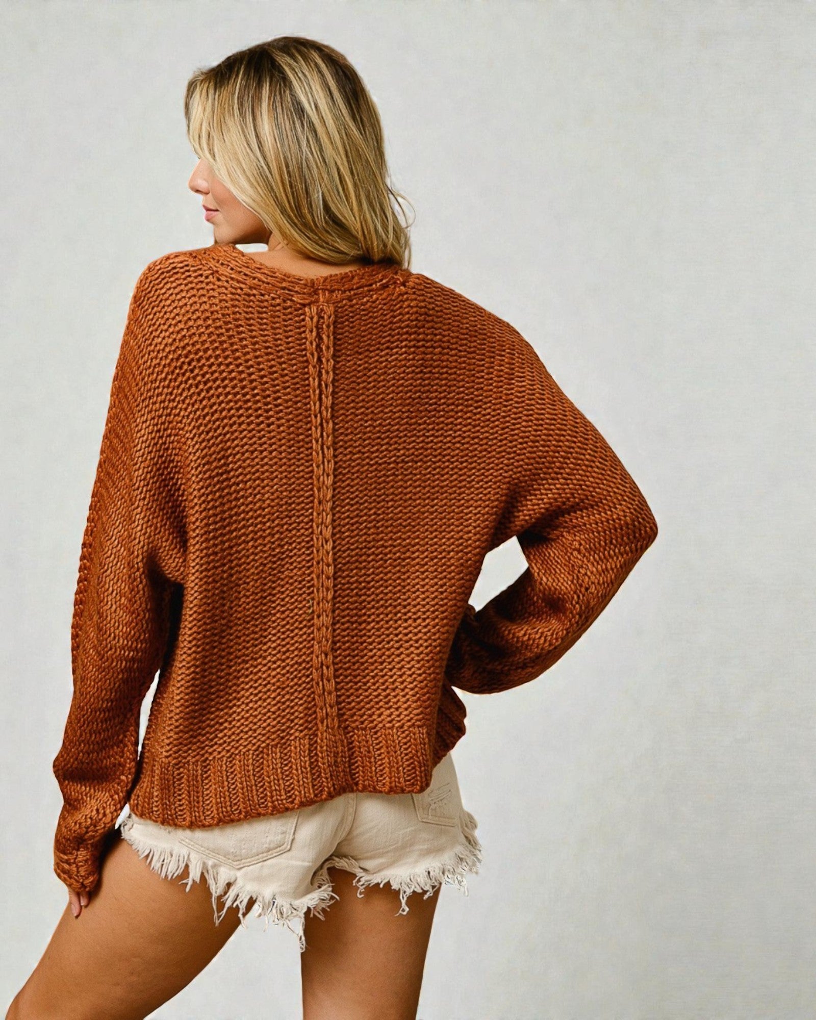 Person wearing a brown knitted sweater and white shorts on a plain background