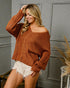 Woman wearing a brown knitted sweater and white shorts indoors.