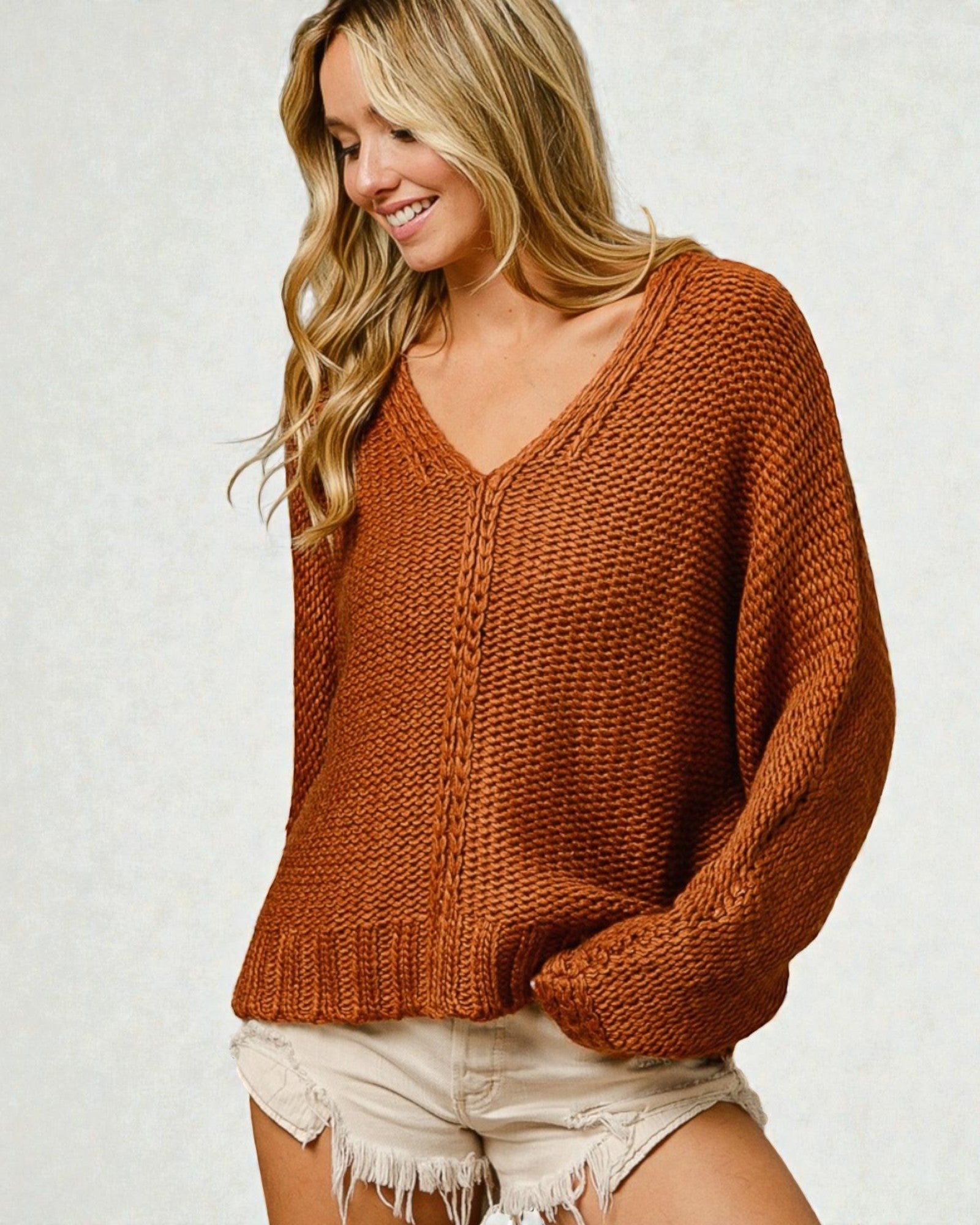 Woman wearing a brown knitted sweater and white shorts on a light background