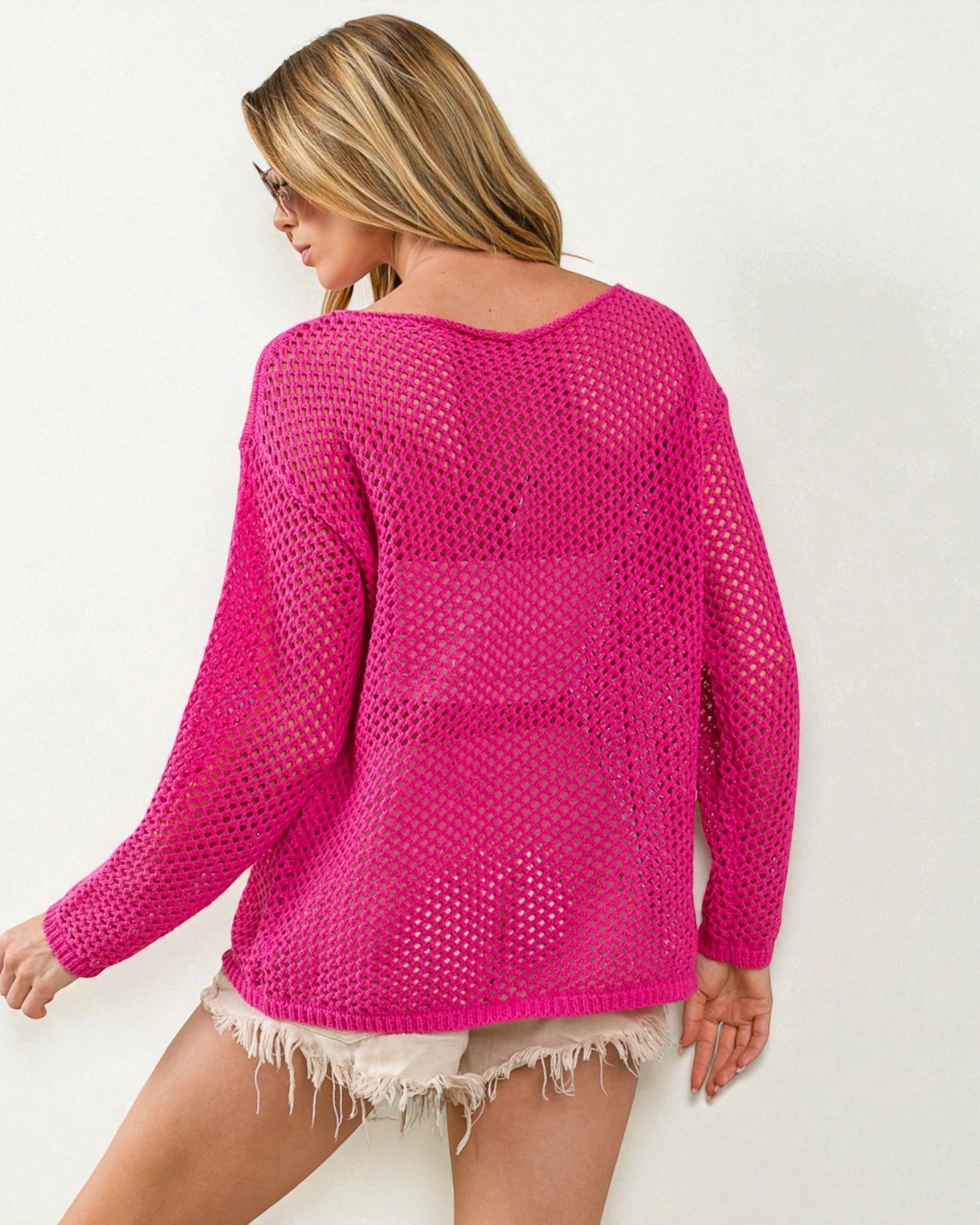 Woman wearing a bright pink crochet sweater on a white background