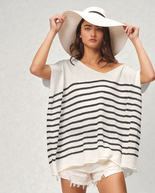 Woman wearing a white and navy striped cover-up with a wide-brimmed hat on a plain background