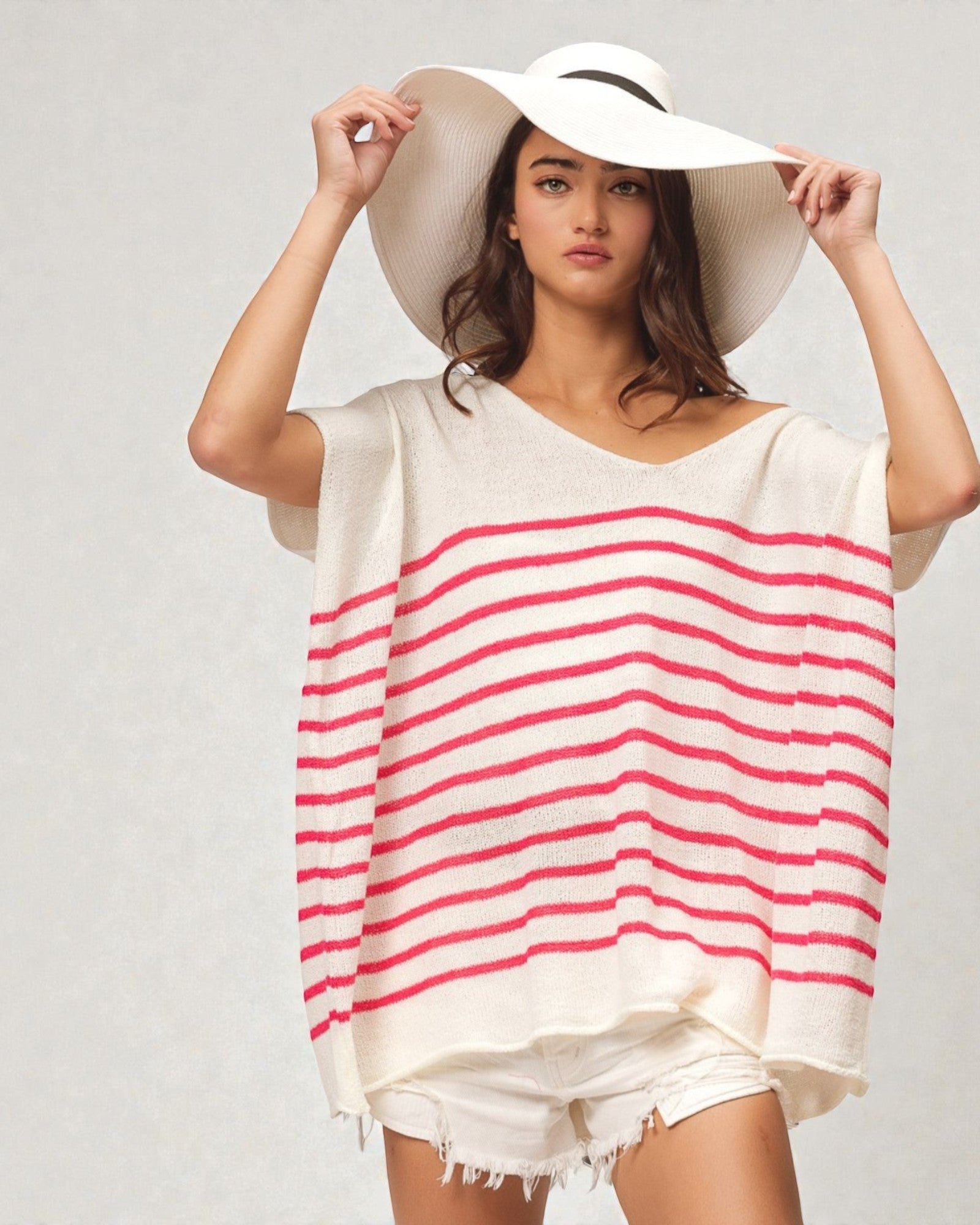 Woman wearing a white and red striped cover-up with a wide-brimmed hat on a plain background