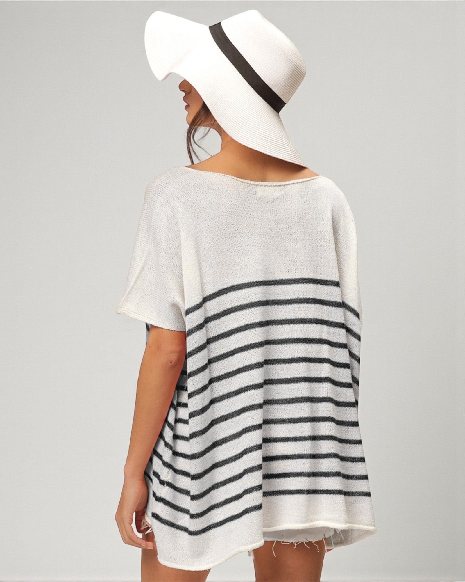 Woman wearing a white and black striped dress with a wide-brimmed hat on a plain background