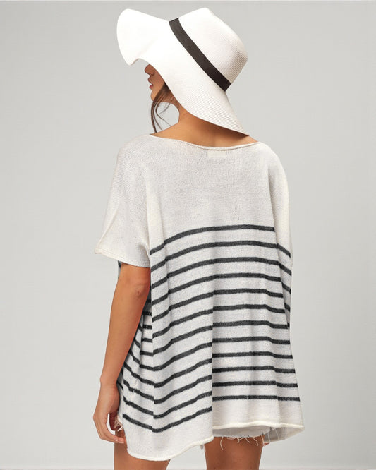 Woman wearing a white and black striped dress with a wide-brimmed hat on a plain background