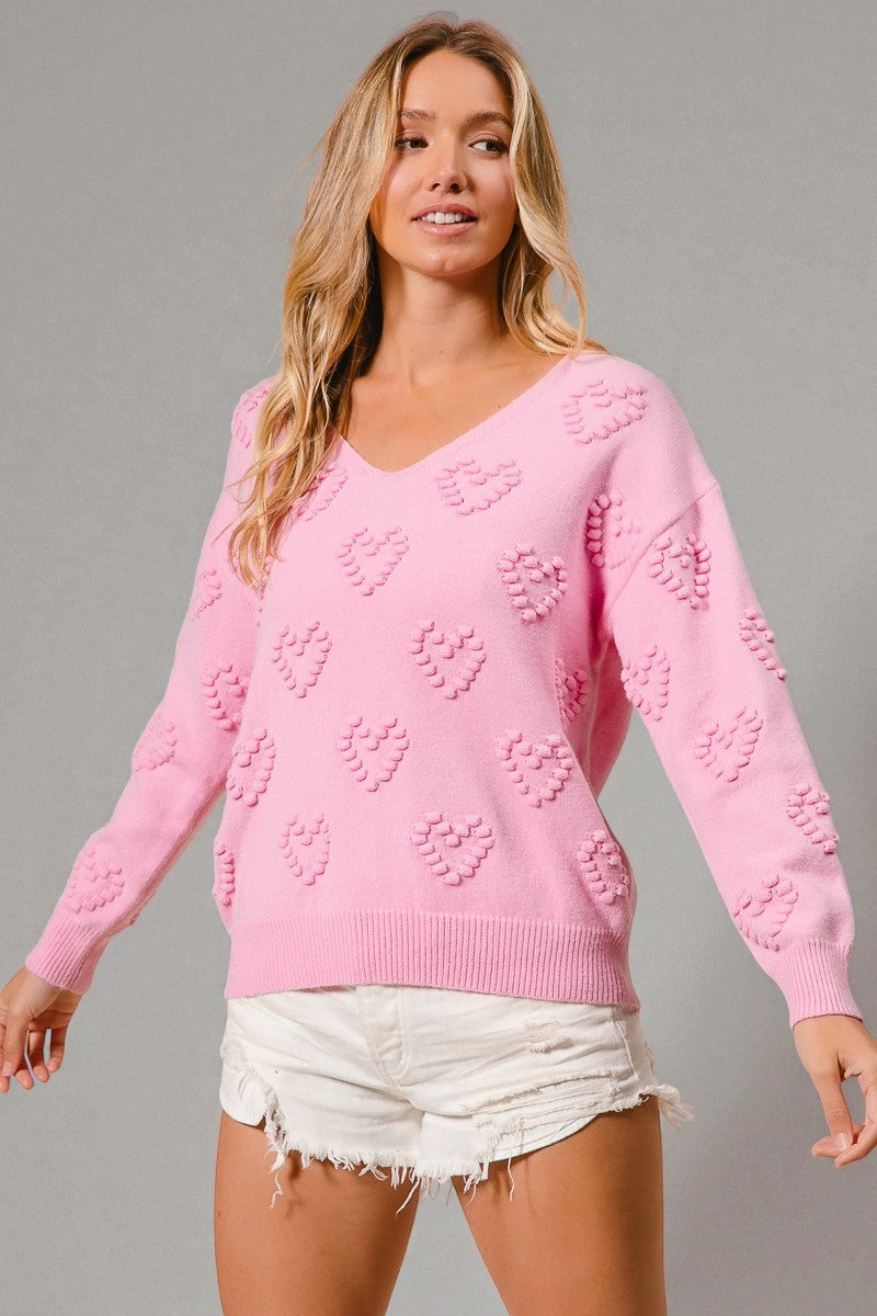 Woman wearing a pink sweater with a pattern against a gray background