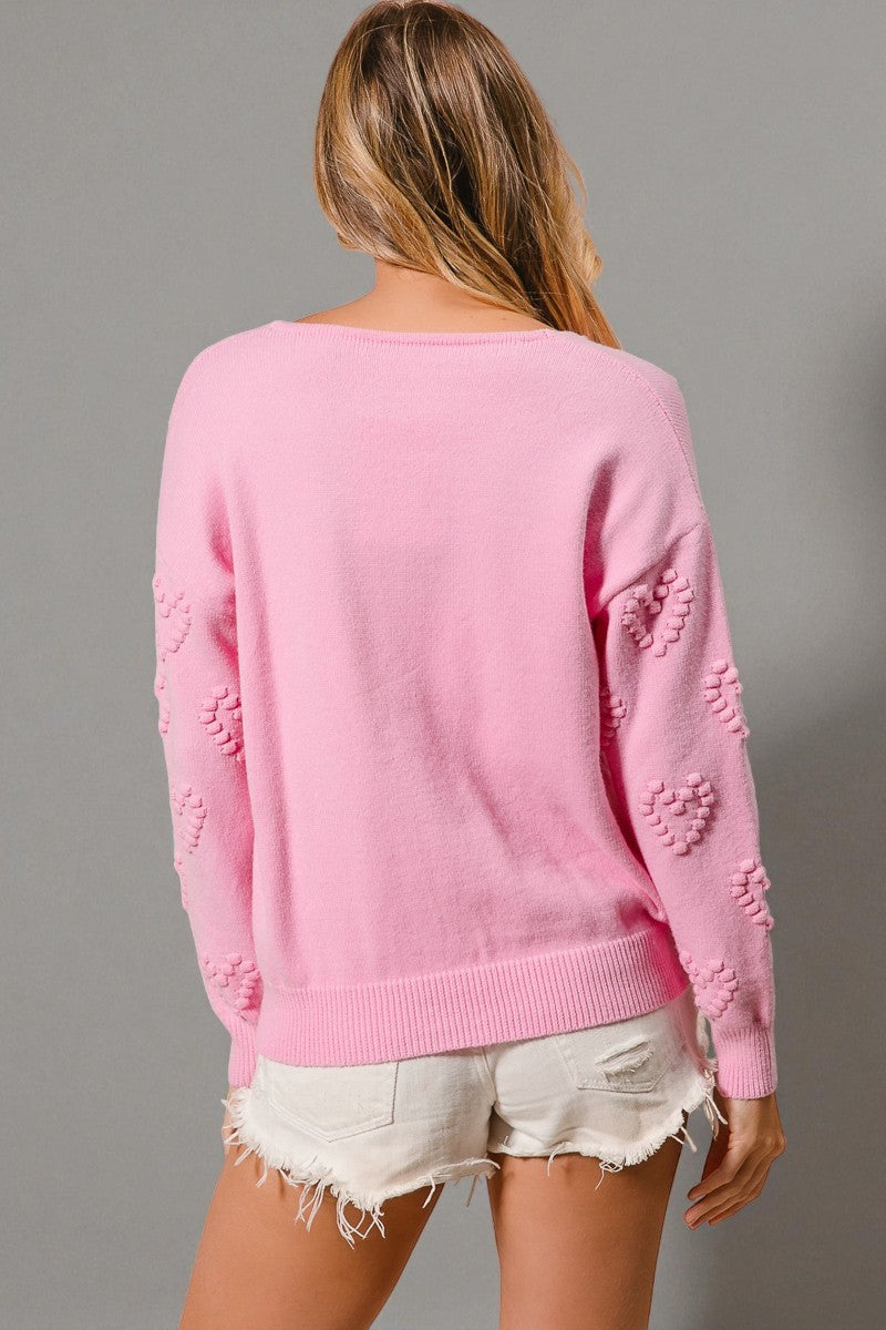 Person wearing a pink sweater with heart patterns on a gray background