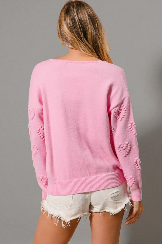 Person wearing a pink sweater with heart patterns on a gray background