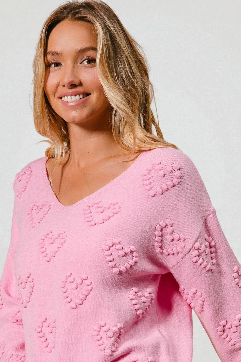Woman wearing a pink sweater with heart patterns against a plain background