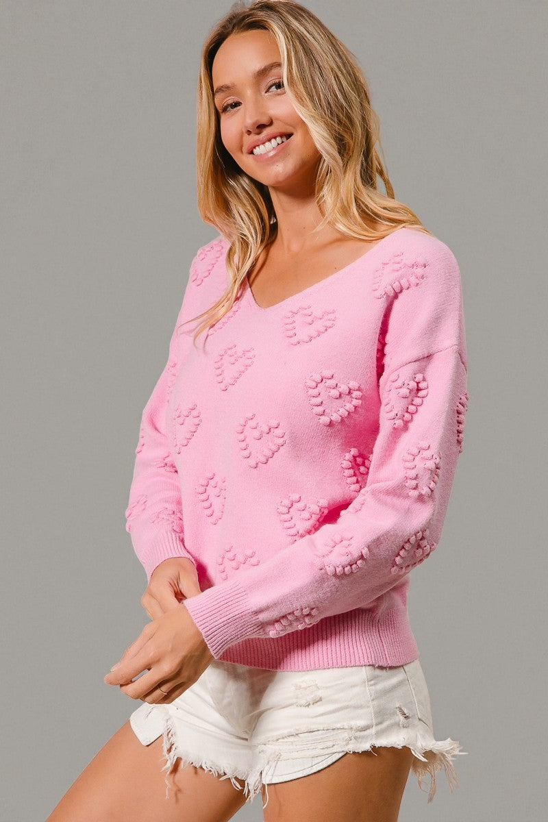 Woman wearing a pink sweater with heart patterns on a gray background