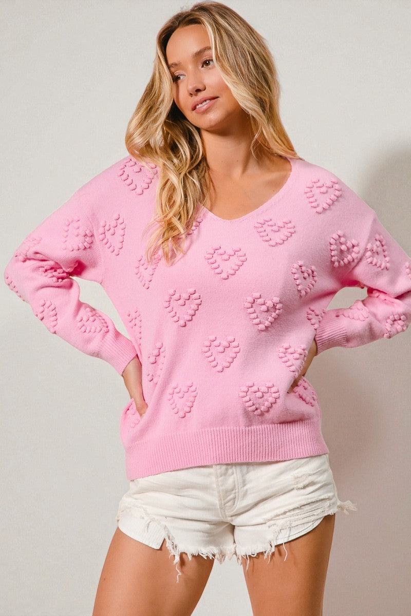 Woman wearing a pink sweater with heart patterns on a plain background