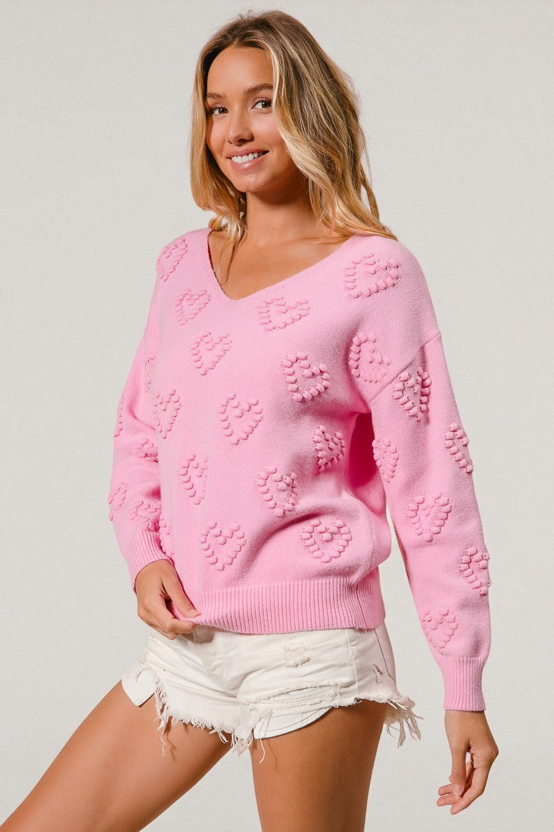 Woman wearing a pink sweater with heart patterns on a plain background