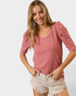 Woman wearing a pink ribbed top and beige shorts on a white background