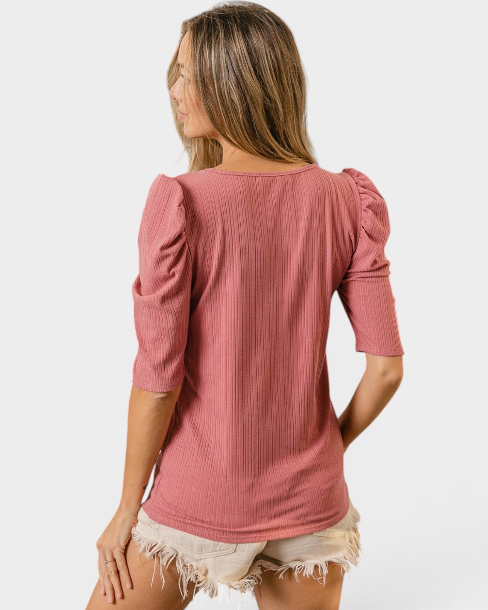 Woman wearing a pink ribbed top with puffed sleeves on a white background