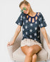 Woman wearing a blue star-patterned top and denim shorts sitting on a white chair.