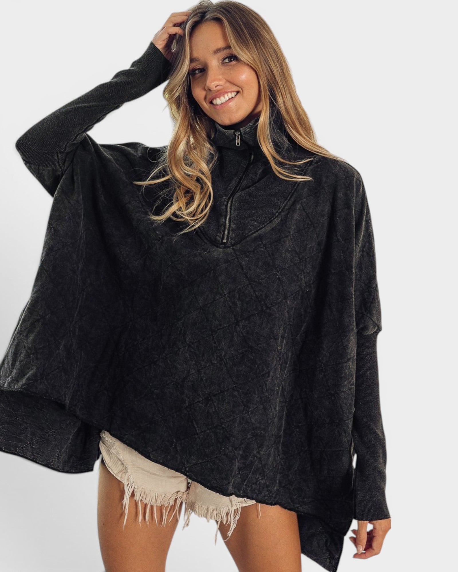 Woman wearing a black poncho over a black long-sleeve shirt on a white background