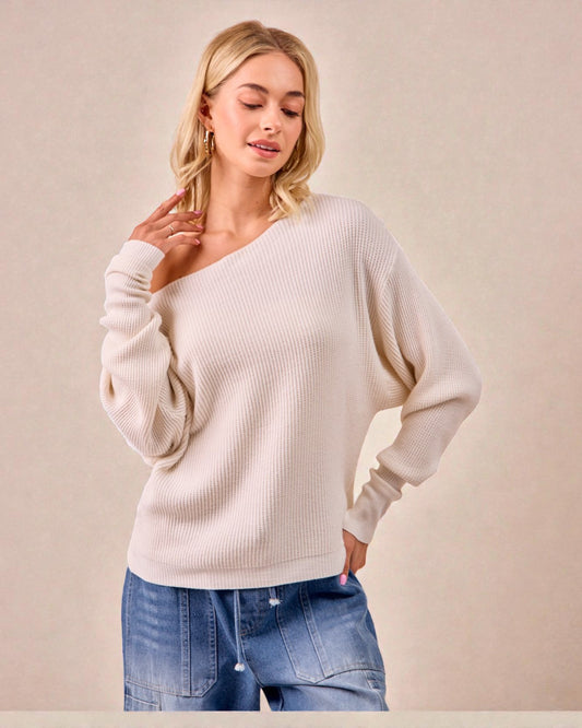 Woman wearing a beige sweater and blue jeans against a plain background