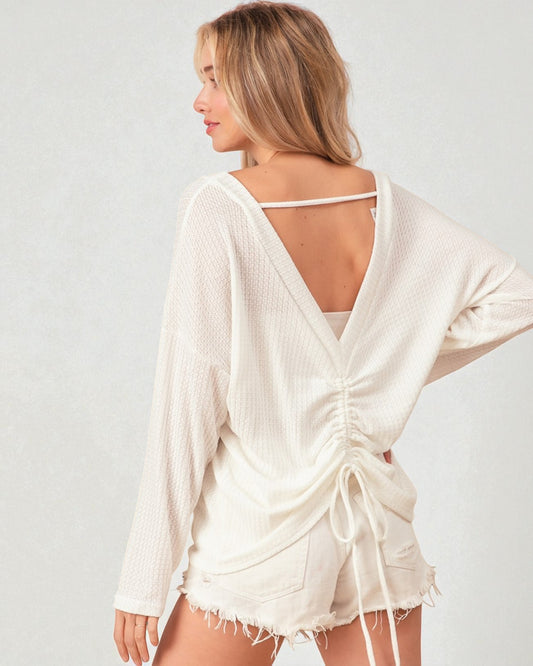 Woman wearing a white open-back top and shorts on a plain background