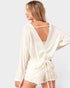 Woman wearing a white open-back cover-up on a plain background