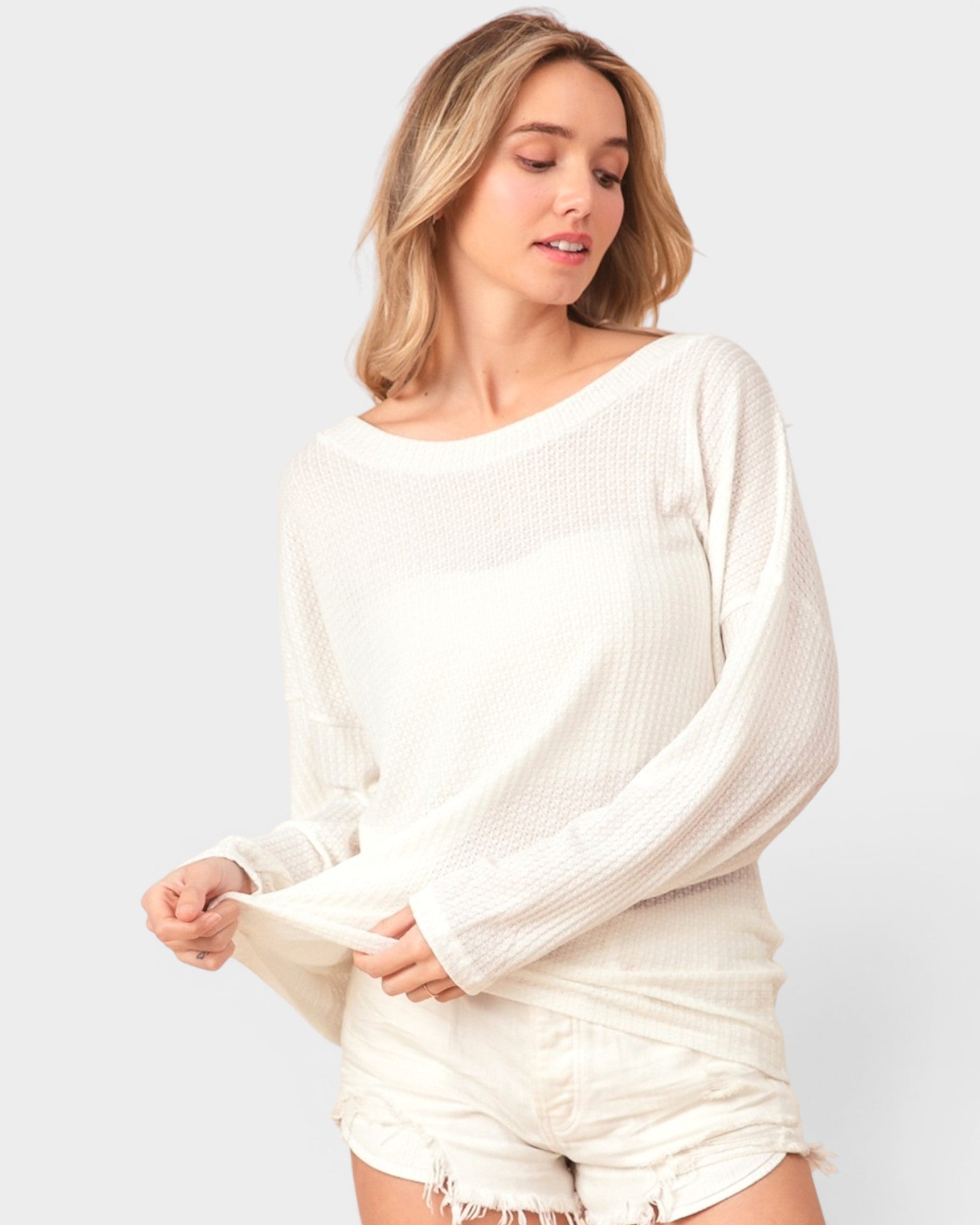 Woman wearing a white ribbed sweater and shorts on a light gray background